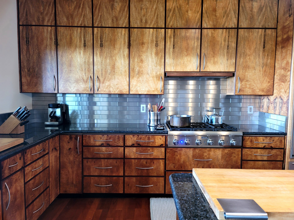 Minimalist medium tone wood floor eat-in kitchen photo in Hawaii with a farmhouse sink, flat-panel cabinets, light wood cabinets, granite countertops, metallic backsplash, metal backsplash, stainless steel appliances, an island and black countertops
