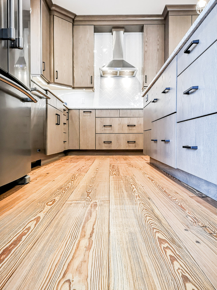 Large transitional u-shaped light wood floor and brown floor eat-in kitchen photo with an undermount sink, flat-panel cabinets, beige cabinets, quartz countertops, white backsplash, subway tile backsplash, stainless steel appliances, an island and white countertops