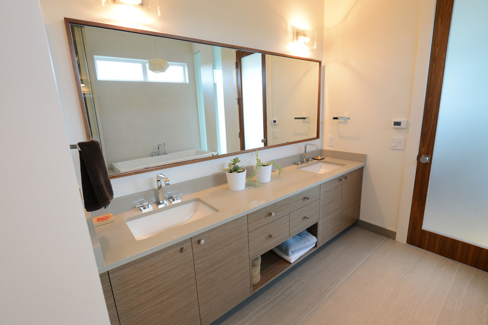 This is an example of a contemporary bathroom in Calgary with a drop-in sink, flat-panel cabinets, light wood cabinets, solid surface benchtops, beige tile and white walls.