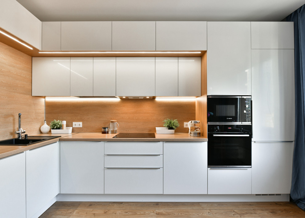 This is an example of a mid-sized contemporary l-shaped kitchen in Saint Petersburg with a drop-in sink, flat-panel cabinets, white cabinets, wood benchtops, brown splashback, timber splashback, panelled appliances, no island, brown floor and beige benchtop.