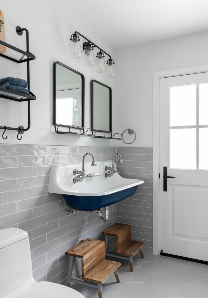 Photo of a mid-sized country kids bathroom in Orange County with blue cabinets, a two-piece toilet, gray tile, mosaic tile, white walls, mosaic tile floors, a wall-mount sink, grey floor, a hinged shower door, a double vanity and a floating vanity.