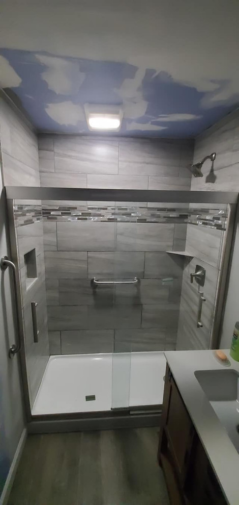 Photo of a medium sized classic shower room bathroom in Other with medium wood cabinets, an alcove shower, a two-piece toilet, grey tiles, ceramic tiles, vinyl flooring, an integrated sink, solid surface worktops, brown floors, a sliding door, white worktops, a wall niche, a single sink and a freestanding vanity unit.