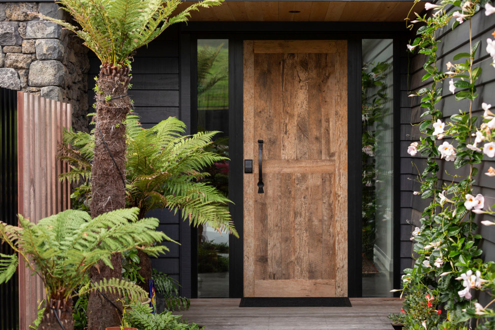 This is an example of a large contemporary front door in Auckland with black walls, light hardwood floors, a single front door, a medium wood front door, beige floor, timber and wood walls.