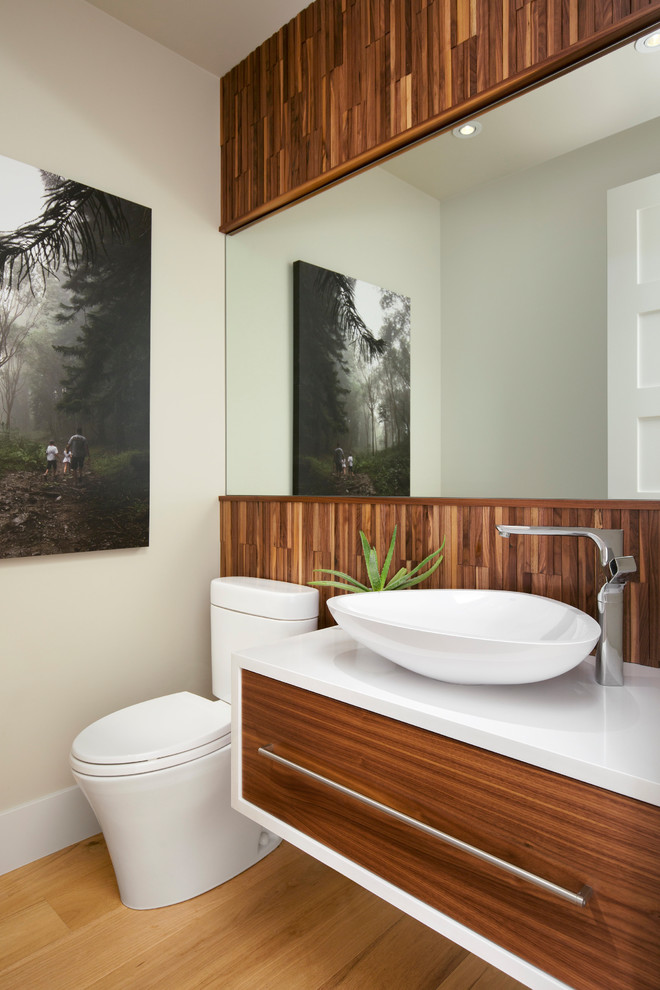 Photo of a modern powder room in Calgary with flat-panel cabinets, medium wood cabinets, a one-piece toilet, white walls, light hardwood floors, a vessel sink and engineered quartz benchtops.