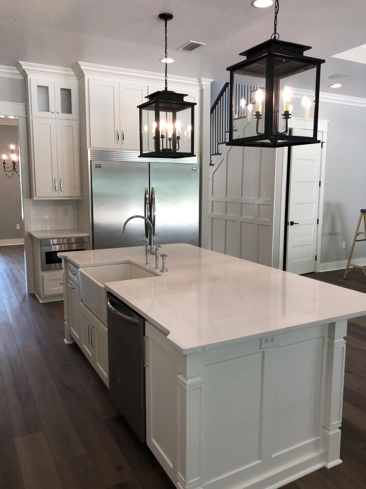 Inspiration for a large country l-shaped eat-in kitchen in Miami with a farmhouse sink, shaker cabinets, white cabinets, quartz benchtops, white splashback, ceramic splashback, stainless steel appliances, medium hardwood floors, with island, brown floor and white benchtop.