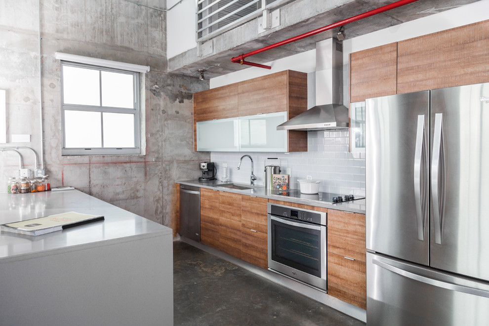 Design ideas for an industrial galley kitchen in Miami with an undermount sink, flat-panel cabinets, medium wood cabinets, grey splashback, subway tile splashback, stainless steel appliances, concrete floors and a peninsula.