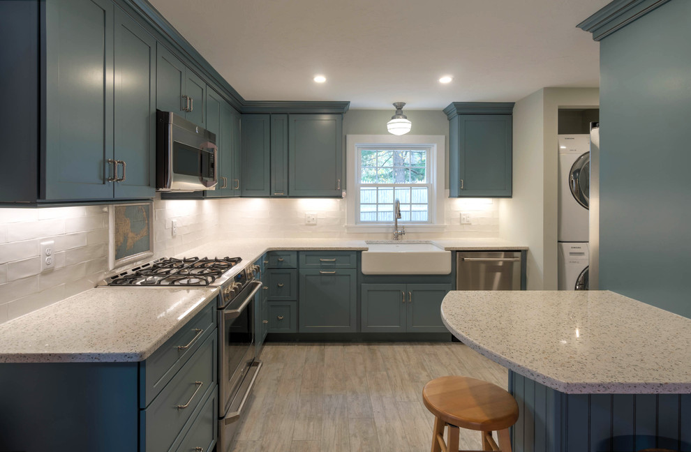 Small modern l-shaped kitchen pantry in Boston with a farmhouse sink, shaker cabinets, blue cabinets, recycled glass benchtops, white splashback, ceramic splashback, stainless steel appliances, ceramic floors, with island and beige floor.