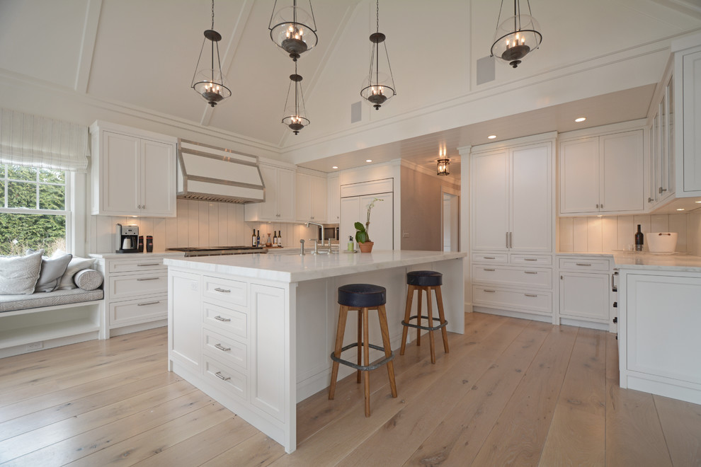 Example of a transitional light wood floor kitchen design in New York with recessed-panel cabinets, white cabinets, white backsplash, stainless steel appliances and an island