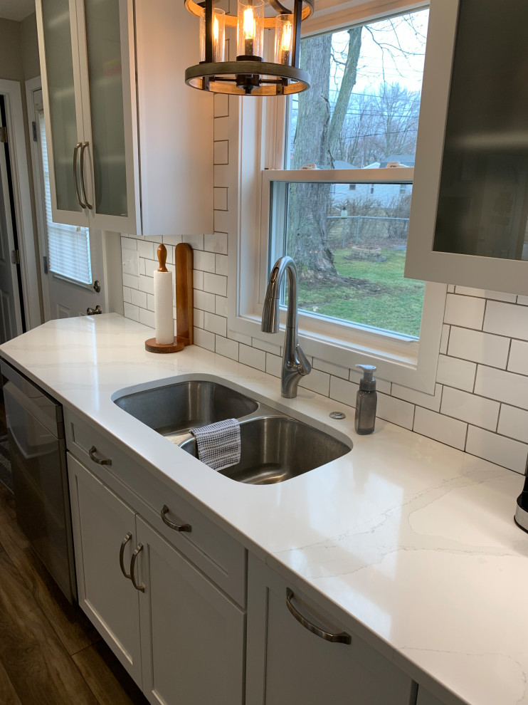 Inspiration for a mid-sized transitional u-shaped vinyl floor and brown floor open concept kitchen remodel with an undermount sink, shaker cabinets, white cabinets, quartz countertops, white backsplash, stainless steel appliances, a peninsula and white countertops
