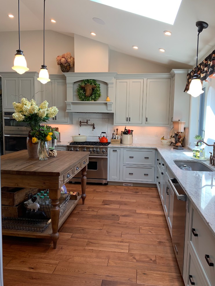 Photo of a mid-sized transitional eat-in kitchen in Boston with a single-bowl sink, beaded inset cabinets, green cabinets, granite benchtops, white splashback, ceramic splashback, stainless steel appliances, dark hardwood floors, with island, brown floor and multi-coloured benchtop.