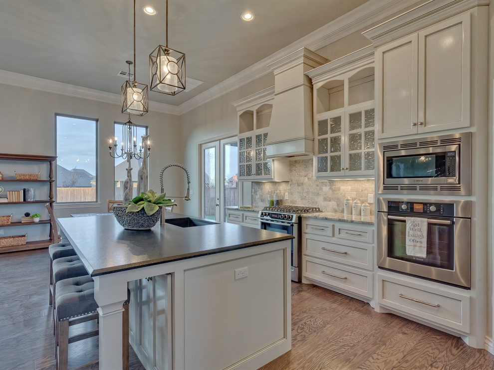 Inspiration for a traditional galley eat-in kitchen in Oklahoma City with an undermount sink, shaker cabinets, beige cabinets, beige splashback, stone tile splashback, medium hardwood floors, with island and brown floor.