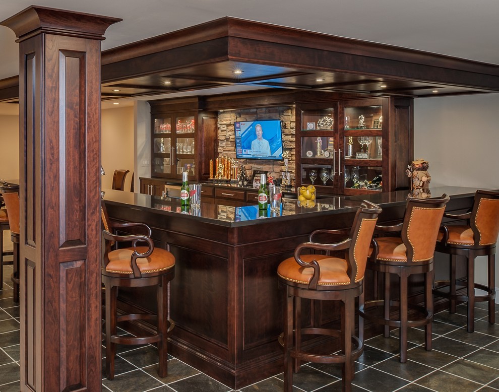Large transitional galley seated home bar in Detroit with an undermount sink, raised-panel cabinets, dark wood cabinets, granite benchtops, beige splashback, stone tile splashback and slate floors.