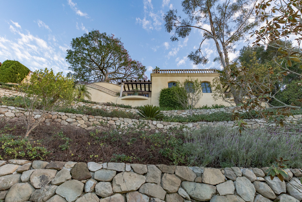 Mediterranean sloped full sun xeriscape in Santa Barbara with a retaining wall and natural stone pavers.