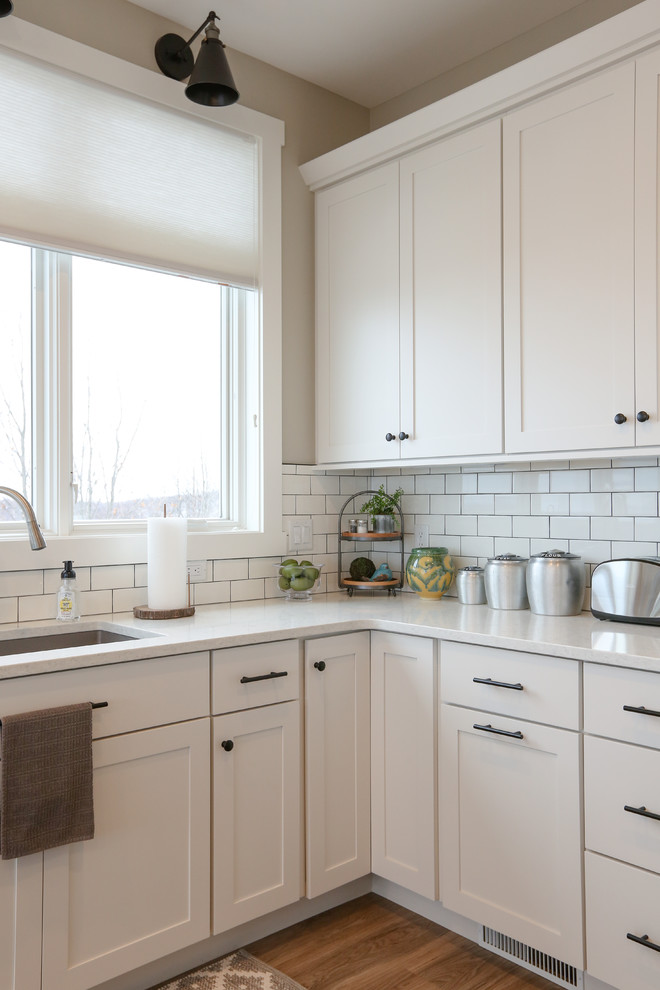 Inspiration for a large transitional u-shaped light wood floor and brown floor eat-in kitchen remodel with an undermount sink, recessed-panel cabinets, white cabinets, quartz countertops, white backsplash, subway tile backsplash, stainless steel appliances, an island and white countertops