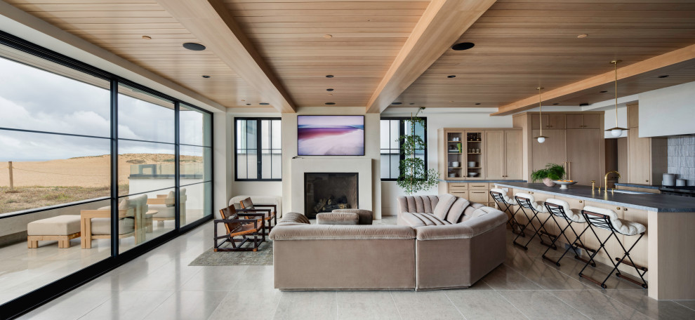 Offenes Maritimes Wohnzimmer mit beiger Wandfarbe, Kamin, TV-Wand, grauem Boden, freigelegten Dachbalken und Holzdecke in Orange County
