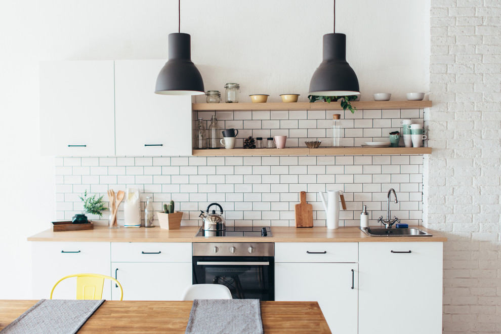 Inspiration for a small scandinavian single-wall kitchen in Other with flat-panel cabinets, white cabinets, laminate benchtops, black appliances, a drop-in sink, white splashback, subway tile splashback and beige benchtop.