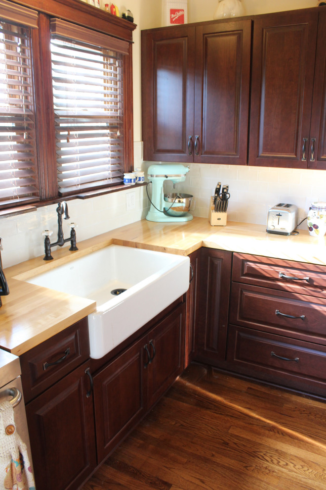 Photo of a small transitional l-shaped separate kitchen in Detroit with a farmhouse sink, raised-panel cabinets, dark wood cabinets, wood benchtops, beige splashback, ceramic splashback, stainless steel appliances, medium hardwood floors, no island, brown floor and yellow benchtop.
