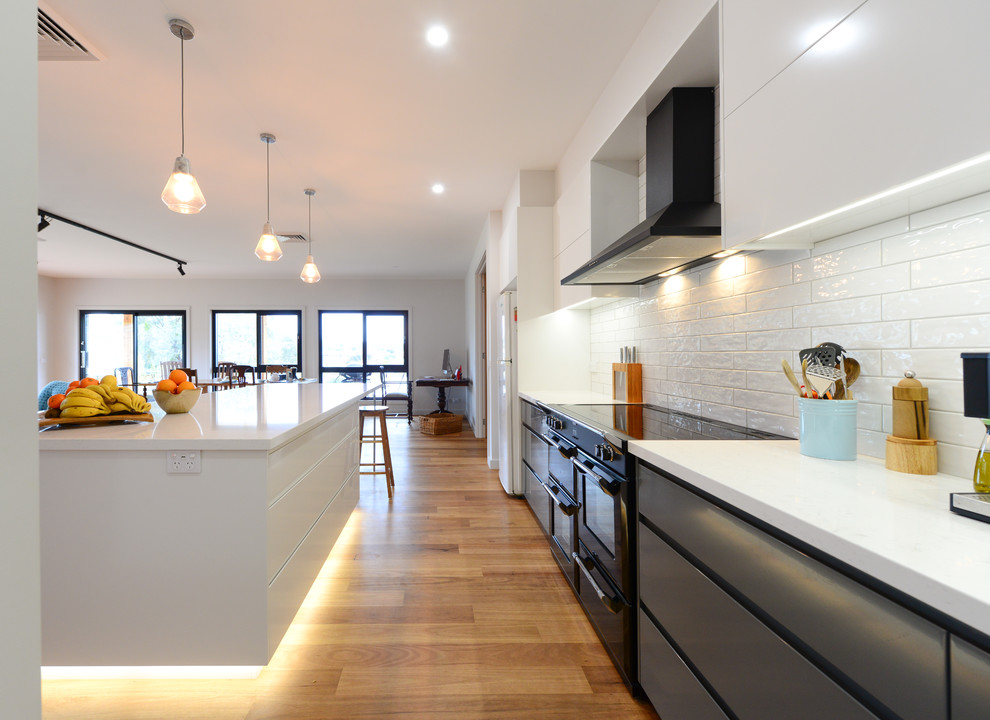 Design ideas for a mid-sized contemporary galley open plan kitchen in Other with a double-bowl sink, grey cabinets, white splashback, subway tile splashback, black appliances, light hardwood floors, with island and brown floor.