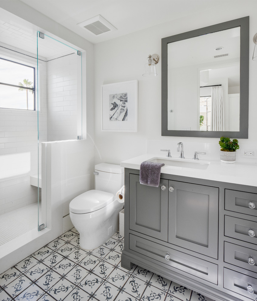 This is an example of a beach style 3/4 bathroom in Orange County with shaker cabinets, grey cabinets, an alcove shower, a one-piece toilet, white tile, subway tile, white walls, an undermount sink, multi-coloured floor and white benchtops.