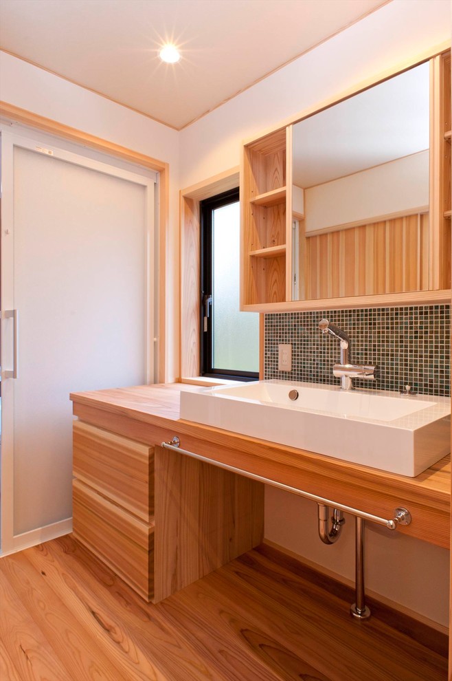 Photo of an asian powder room in Other with medium wood cabinets, multi-coloured tile, white walls, medium hardwood floors, a vessel sink, wood benchtops, brown floor and brown benchtops.