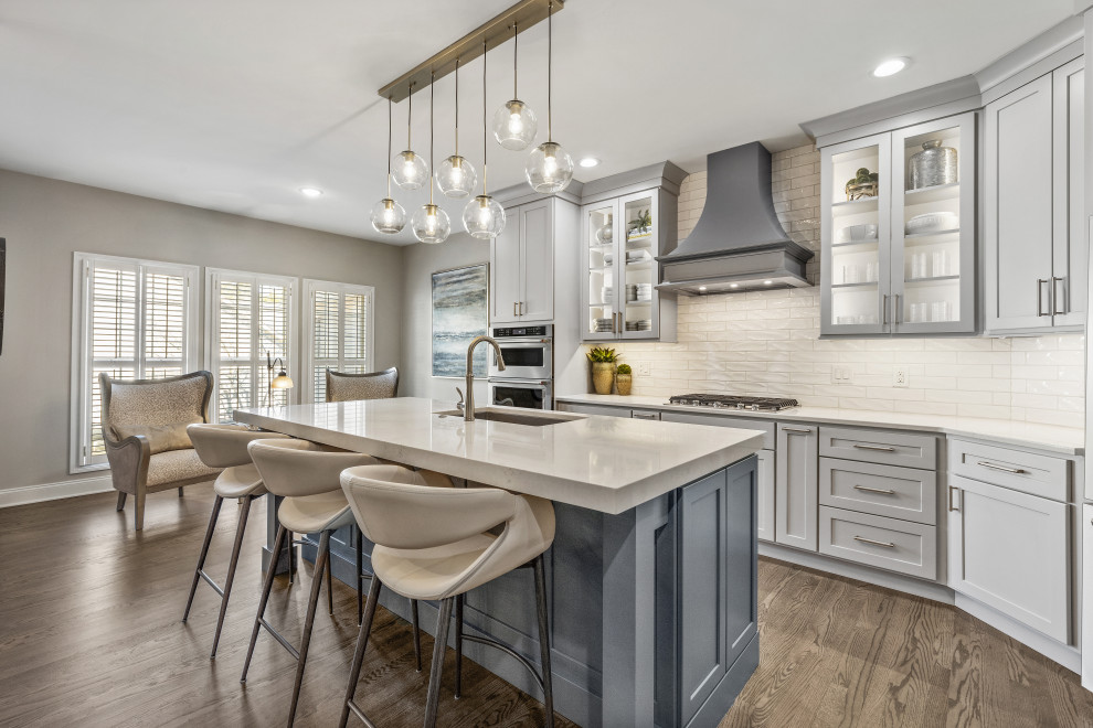 Inspiration for a mid-sized transitional medium tone wood floor and brown floor kitchen remodel with an undermount sink, recessed-panel cabinets, quartz countertops, white backsplash, subway tile backsplash, stainless steel appliances, an island and white countertops