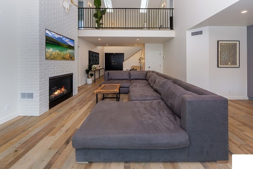 Large industrial formal open concept living room in Los Angeles with white walls, plywood floors, a ribbon fireplace, a brick fireplace surround, a wall-mounted tv and multi-coloured floor.