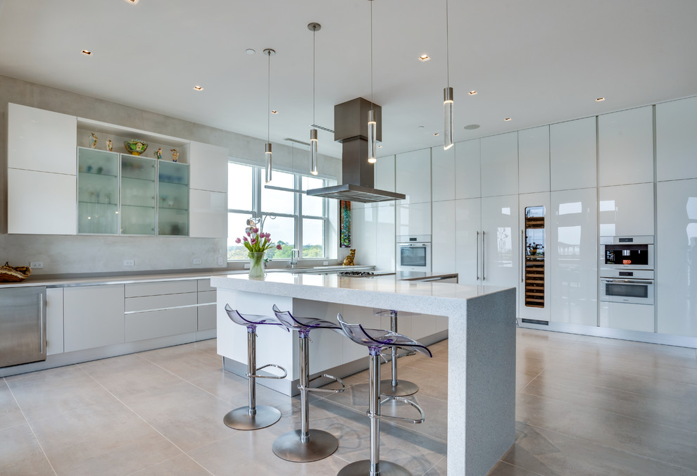 Photo of a contemporary eat-in kitchen in Miami with an undermount sink, flat-panel cabinets, white cabinets, quartz benchtops, white splashback, stone slab splashback, white appliances, porcelain floors, with island and beige floor.