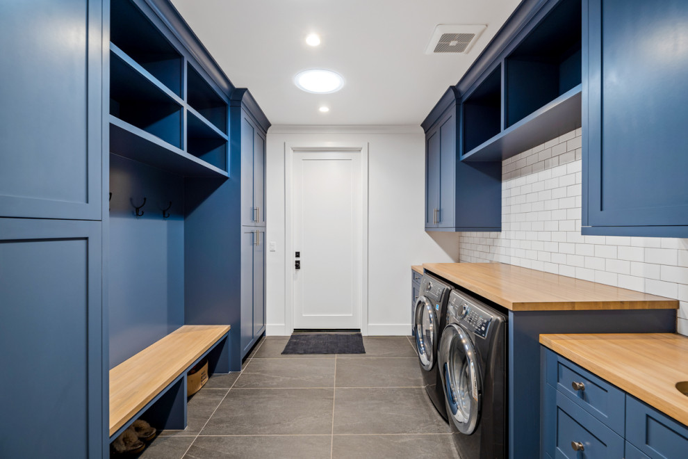 Inspiration for an expansive country galley utility room in Los Angeles with an undermount sink, shaker cabinets, blue cabinets, wood benchtops, white splashback, ceramic splashback, white walls, porcelain floors, a side-by-side washer and dryer, grey floor and beige benchtop.