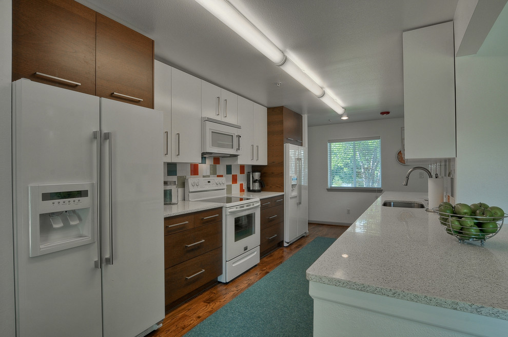 This is an example of a mid-sized midcentury galley eat-in kitchen in Dallas with flat-panel cabinets, medium wood cabinets, quartz benchtops, multi-coloured splashback, ceramic splashback, white appliances, medium hardwood floors, a peninsula and an undermount sink.
