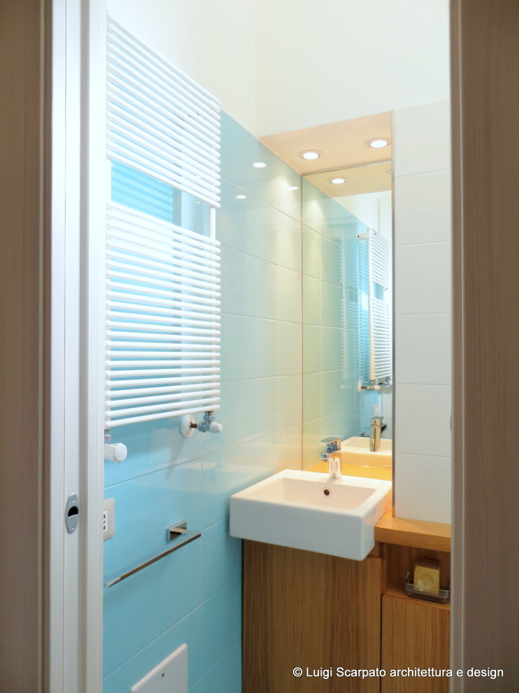 Small contemporary powder room in Naples with flat-panel cabinets, medium wood cabinets, a one-piece toilet, blue tile, ceramic tile, white walls, ceramic floors, a drop-in sink, wood benchtops and blue floor.