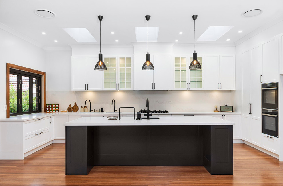 Design ideas for a large traditional u-shaped eat-in kitchen in Sydney with an undermount sink, shaker cabinets, yellow cabinets, quartz benchtops, white splashback, engineered quartz splashback, stainless steel appliances, medium hardwood floors, with island, brown floor and white benchtop.