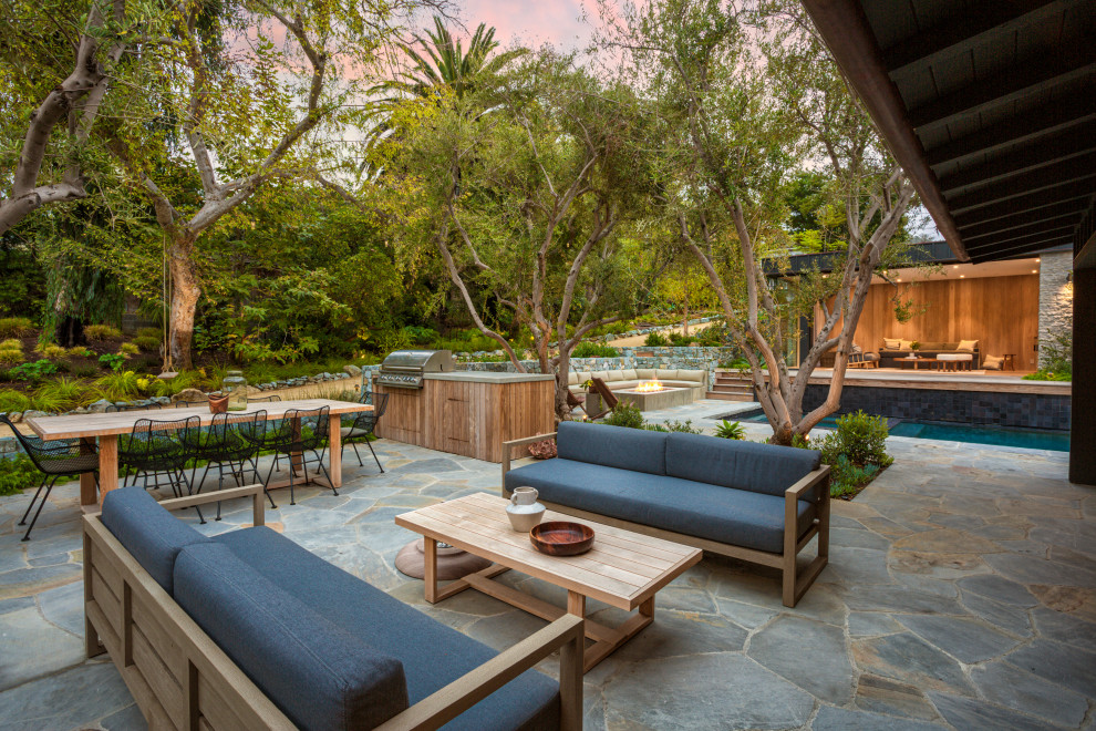 Inspiration for a contemporary backyard patio in Orange County with natural stone pavers and a roof extension.