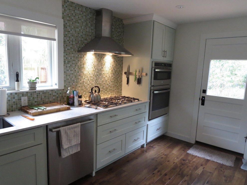 Example of a mid-sized transitional medium tone wood floor eat-in kitchen design in Austin with shaker cabinets, glass tile backsplash, stainless steel appliances, a single-bowl sink, green cabinets, quartz countertops, green backsplash and a peninsula