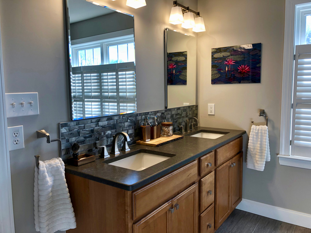 This is an example of a mid-sized transitional master bathroom in Philadelphia with shaker cabinets, medium wood cabinets, a curbless shower, a two-piece toilet, gray tile, glass tile, grey walls, porcelain floors, an undermount sink, grey floor, a hinged shower door and grey benchtops.