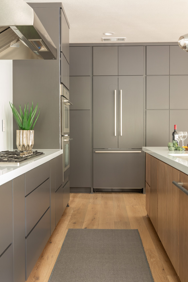 Immagine di una cucina minimalista di medie dimensioni con ante lisce, ante grigie, top in quarzo composito, elettrodomestici in acciaio inossidabile, pavimento in legno massello medio e top bianco