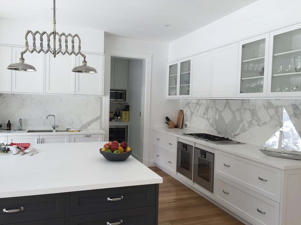 Design ideas for a large modern l-shaped open plan kitchen in Sydney with a double-bowl sink, shaker cabinets, white cabinets, quartz benchtops, white splashback, marble splashback, stainless steel appliances, light hardwood floors and with island.