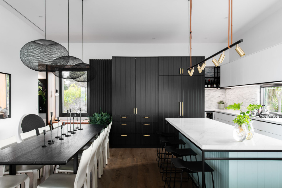 Moderne Küche in L-Form mit flächenbündigen Schrankfronten, weißen Schränken, Küchenrückwand in Grau, Rückwand aus Mosaikfliesen, Elektrogeräten mit Frontblende, dunklem Holzboden, Kücheninsel, braunem Boden und weißer Arbeitsplatte in Hobart