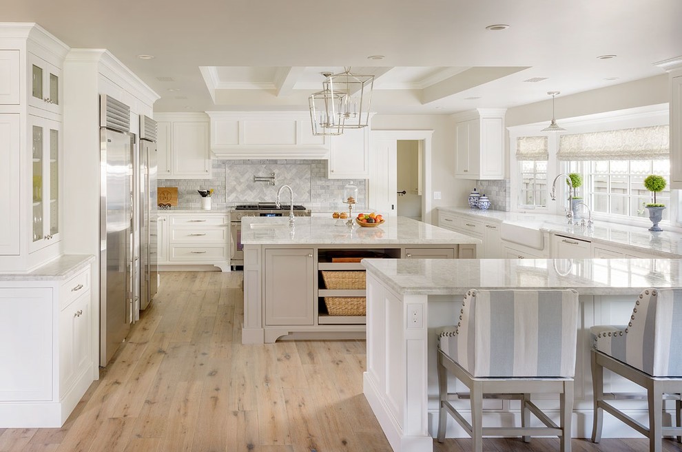 Large country u-shaped eat-in kitchen in San Diego with a farmhouse sink, shaker cabinets, white cabinets, quartzite benchtops, grey splashback, marble splashback, stainless steel appliances, light hardwood floors, with island and beige floor.
