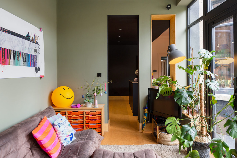 Пример оригинального дизайна: маленькая открытая гостиная комната в современном стиле с с книжными шкафами и полками, зелеными стенами, пробковым полом и отдельно стоящим телевизором для на участке и в саду