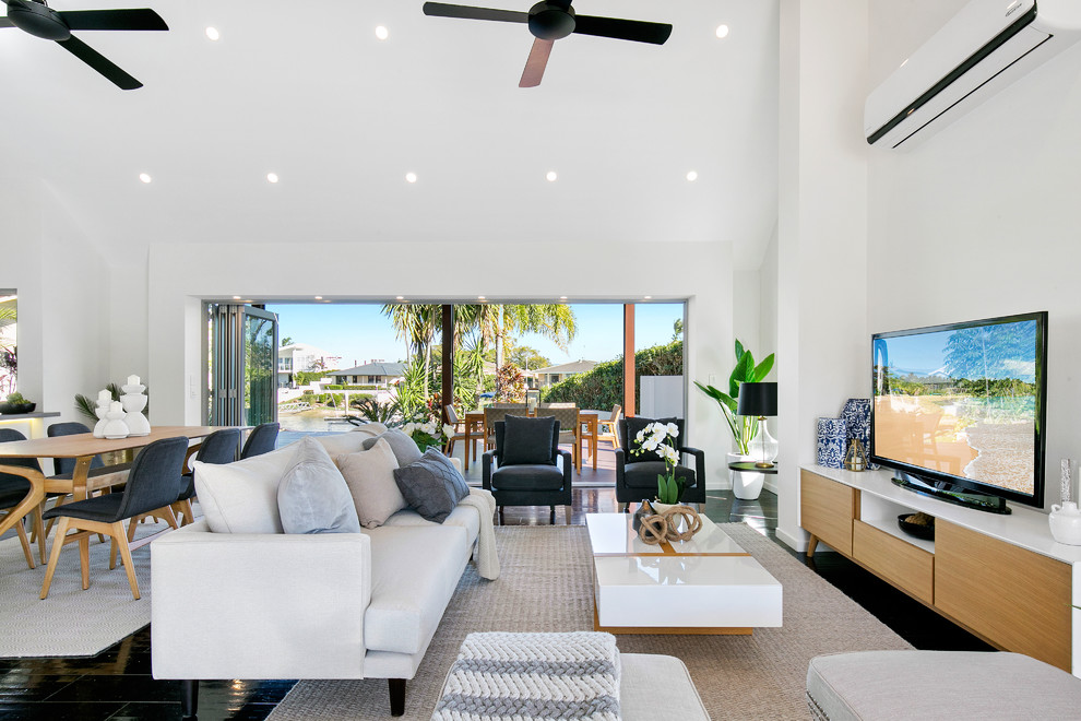 This is an example of a beach style formal open concept living room in Brisbane with white walls, a freestanding tv and black floor.