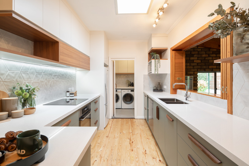 Mid-sized contemporary galley kitchen pantry in Adelaide with an undermount sink, flat-panel cabinets, green cabinets, quartz benchtops, grey splashback, porcelain splashback, stainless steel appliances, light hardwood floors, a peninsula and white benchtop.
