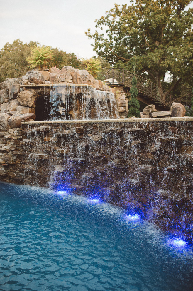 Photo of a large arts and crafts backyard custom-shaped pool in Kansas City with a water feature and natural stone pavers.