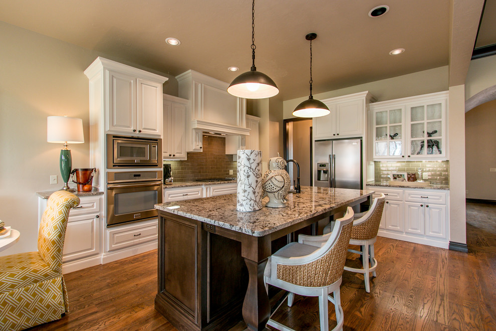 This is an example of a mid-sized traditional l-shaped eat-in kitchen in Oklahoma City with raised-panel cabinets, white cabinets, stainless steel appliances, dark hardwood floors, with island, an undermount sink, granite benchtops, green splashback, subway tile splashback and brown floor.