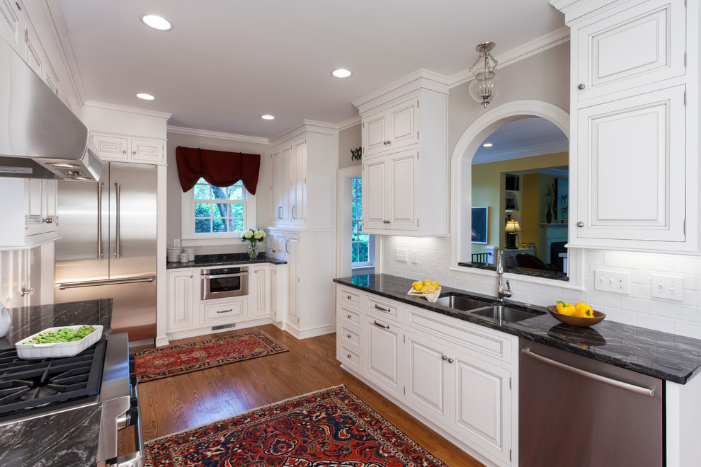 Inspiration for a large transitional u-shaped separate kitchen in Charlotte with raised-panel cabinets, white cabinets, white splashback, subway tile splashback, stainless steel appliances, medium hardwood floors, no island, a double-bowl sink and marble benchtops.