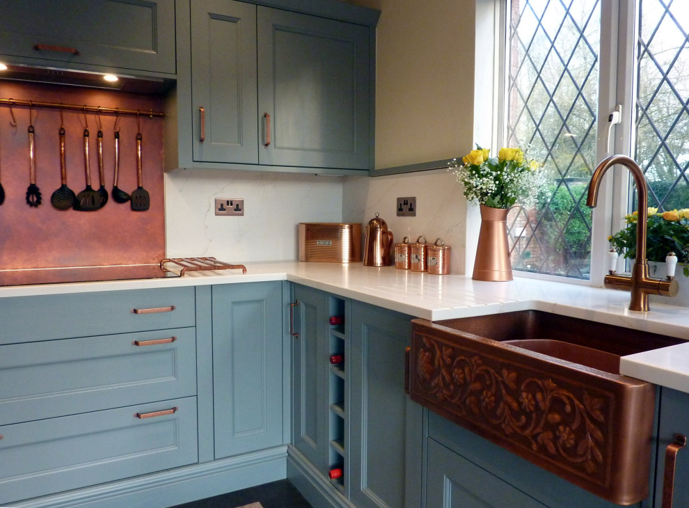Photo of a large transitional galley eat-in kitchen in West Midlands with a farmhouse sink, beaded inset cabinets, blue cabinets, quartzite benchtops, orange splashback, black appliances, vinyl floors, with island, grey floor, white benchtop and exposed beam.