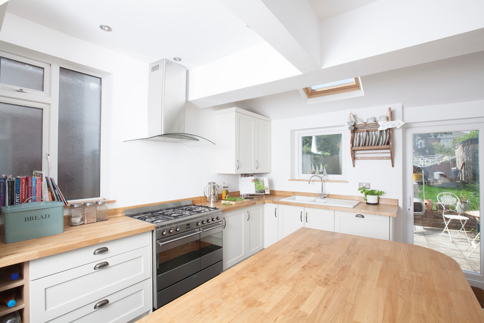Inspiration for a beach style eat-in kitchen in Cardiff with a drop-in sink, shaker cabinets, white cabinets, wood benchtops, stainless steel appliances, slate floors and with island.