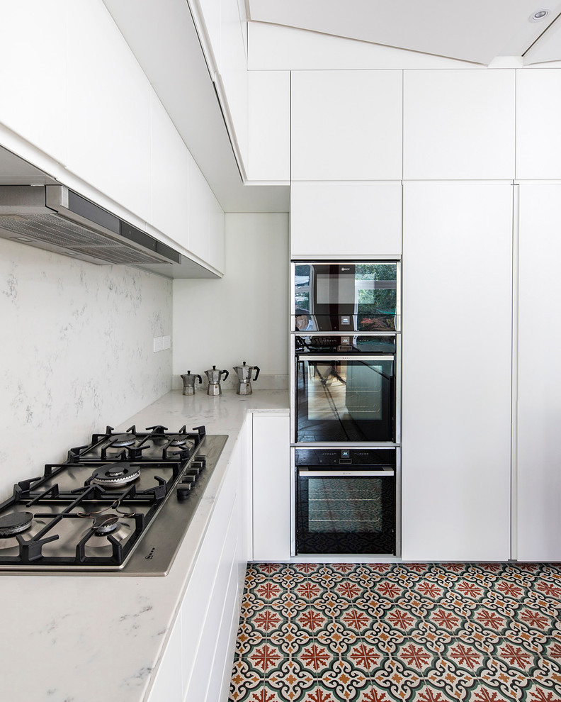 Photo of a contemporary kitchen in London with flat-panel cabinets, white cabinets, marble benchtops, white splashback, marble splashback, stainless steel appliances, ceramic floors, multi-coloured floor and white benchtop.