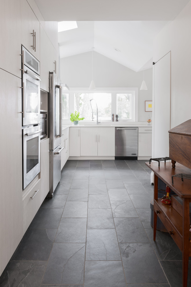Inspiration for a mid-sized modern u-shaped eat-in kitchen in Boston with a double-bowl sink, flat-panel cabinets, white cabinets, marble benchtops, white splashback, marble splashback, stainless steel appliances, slate floors, no island and black floor.