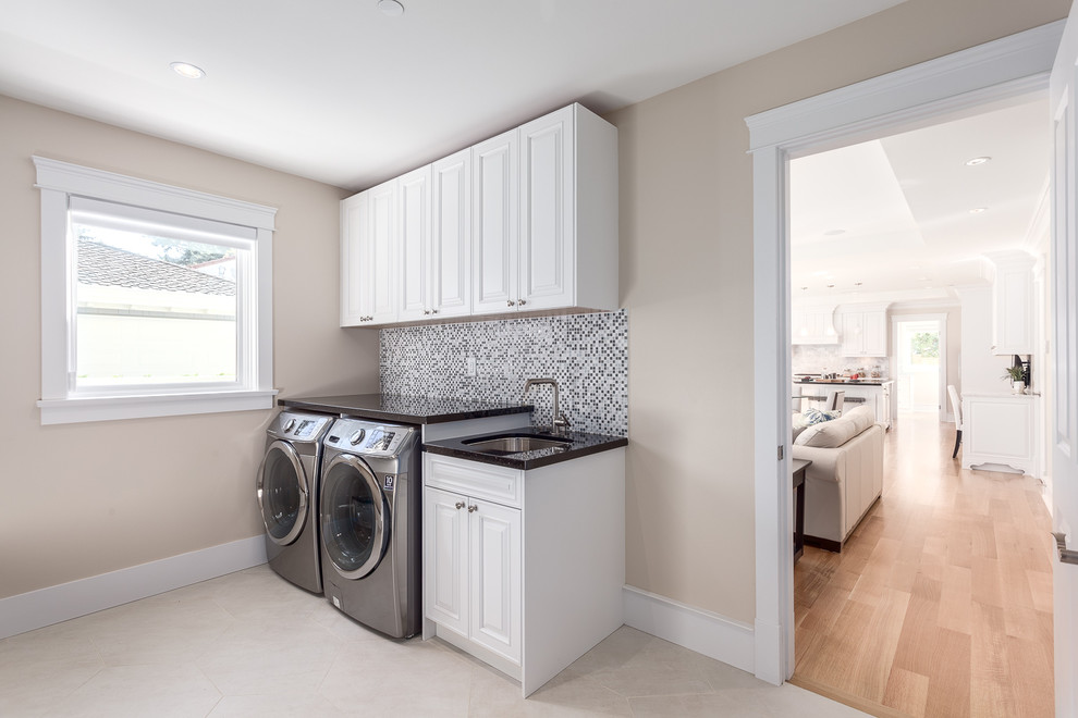 Inspiration for a large transitional single-wall dedicated laundry room in Vancouver with white cabinets, beige walls, a side-by-side washer and dryer, an undermount sink, raised-panel cabinets, granite benchtops and travertine floors.