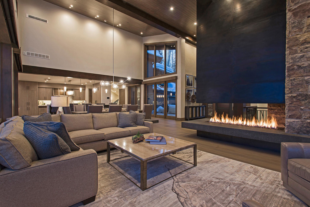 Inspiration for an expansive contemporary formal open concept living room in Salt Lake City with grey walls, medium hardwood floors, a two-sided fireplace, a metal fireplace surround, no tv and wood.